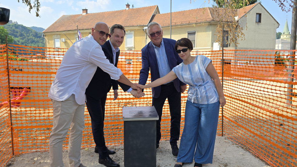 Župan Celja Kovač in minister Novak s sodelavci stojita na gradbišču pred temeljnim kamnom za nov most