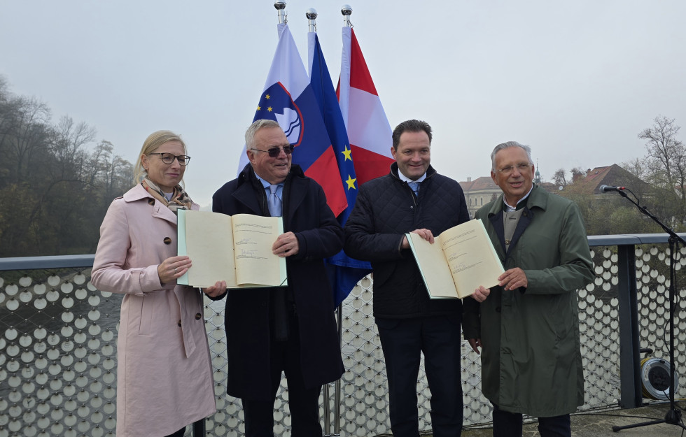 Ministra Novak in Totschnig stojita na mostu na Muri in v rokah držita podpisani deklaraciji