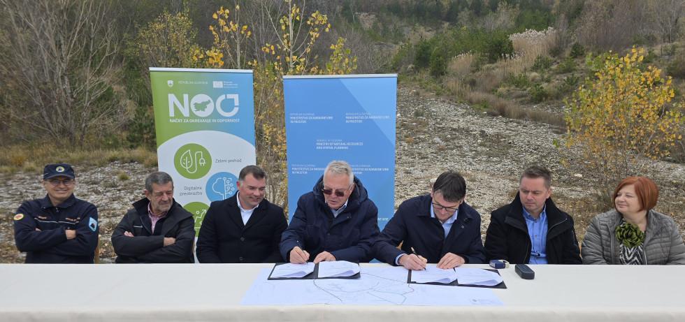 Minister Novak sedi pred deloviščem in podpisuje pogodbo