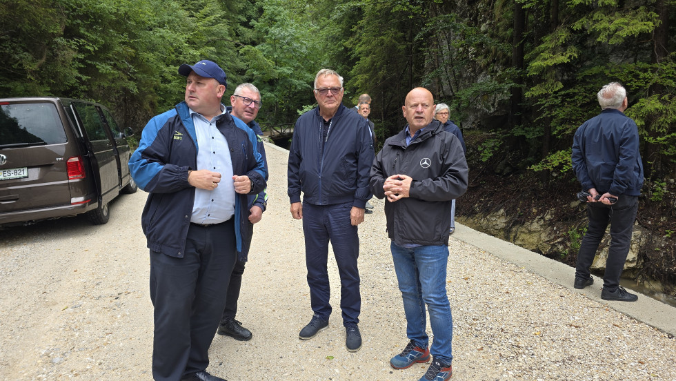 Minister in predstavniki občin stojijo ob strugi potoka in si ogledujejo opravljeno delo.