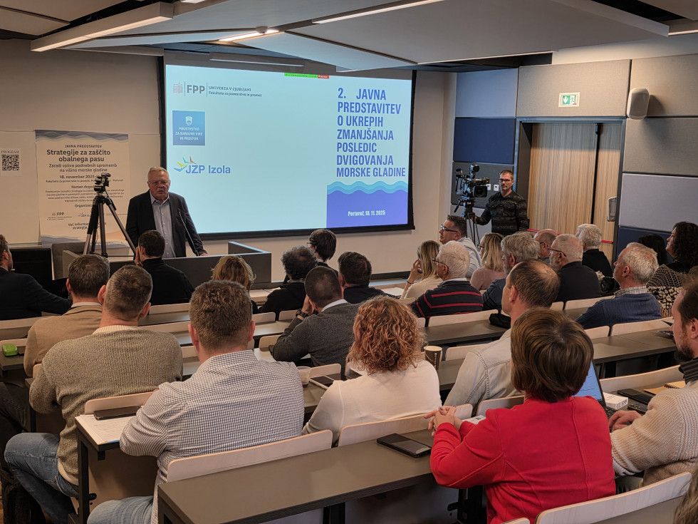 Minister stoji pred publiko in nagovarja zbrane