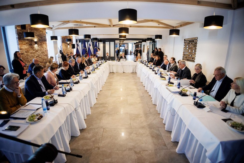 Predstavniki vlade sedijo v veliki sejni sobi levo in desno za mizami na redni seji vlade na terenskem obisku v Savinjski regiji