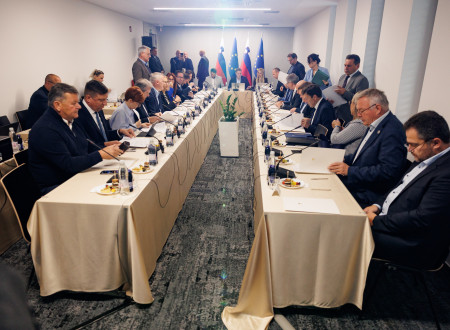 Ministri sedijo za podolgovato mizo, v ozadju predsednik vlade s sodelavci