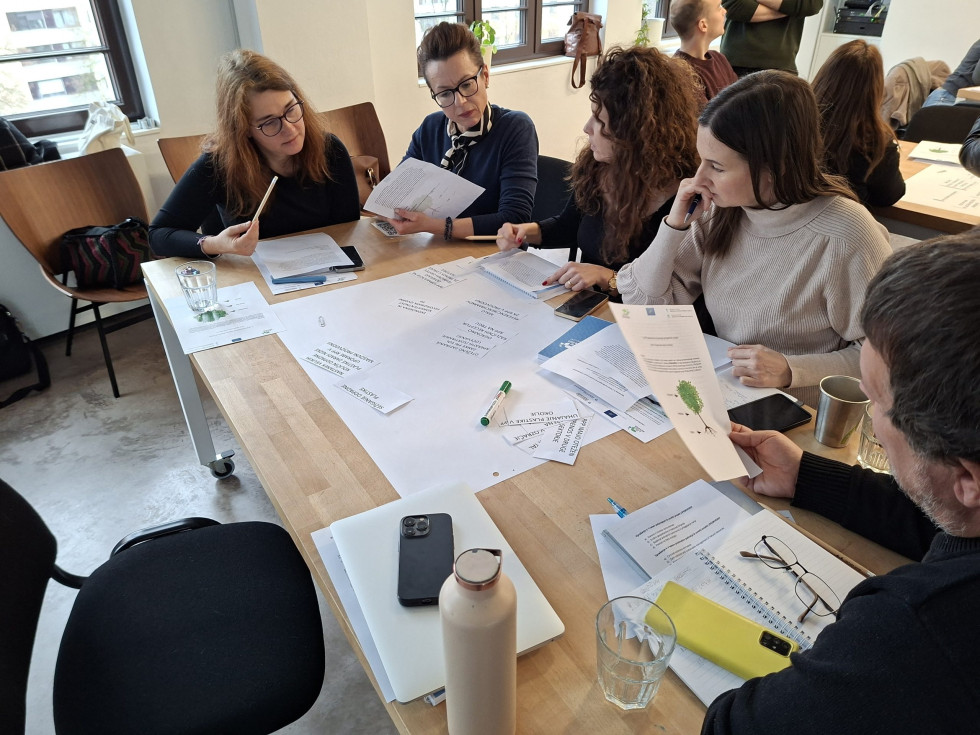 Udeleženci delavnice sedijo za mizo in razpravljajo ter zapisujejo predloge