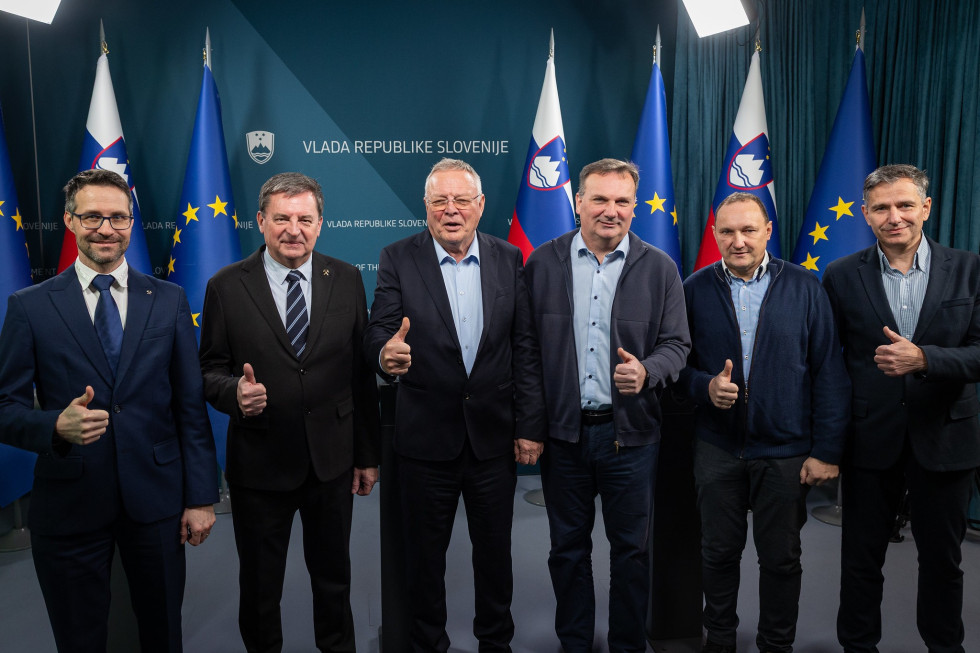 Minister Novak in predstavniki premogovnika Velenje stojijo pred zastavami v vladnem novinarskem središču