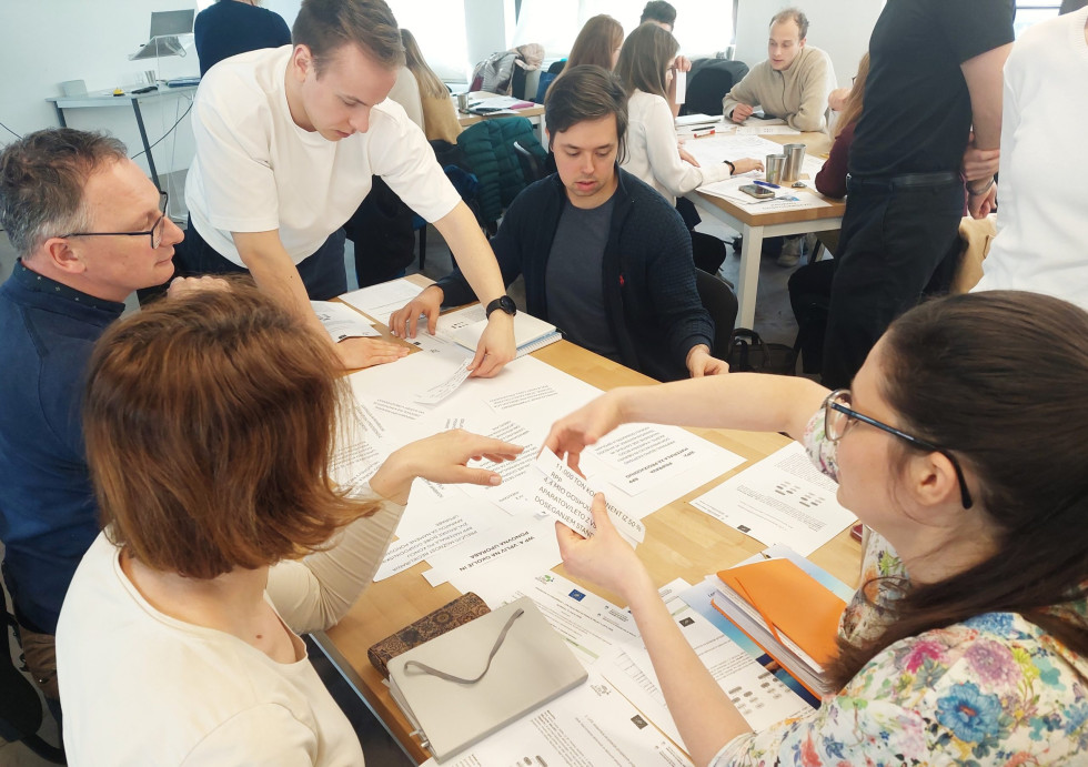 Udeleženci delavnice sedijo za mizo in pišejo predloge ter rešitve