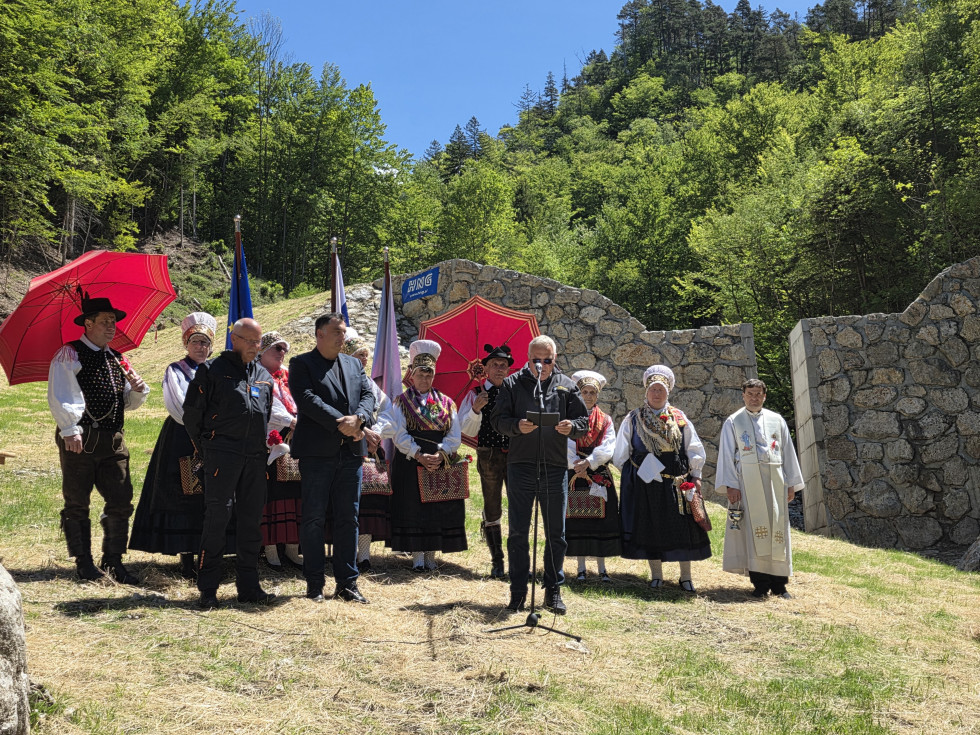 Minister Novak ima uvodni nagovor pred zgrajenim objektom nad plazom. V ozadju moški in ženske oblečeni v slovenske narodne noše.