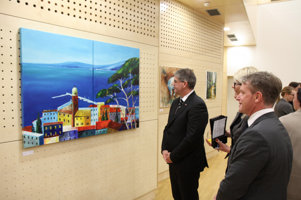 Minister Boštjan Poklukar si ogleduje sliko, na sliki hiše ob morju