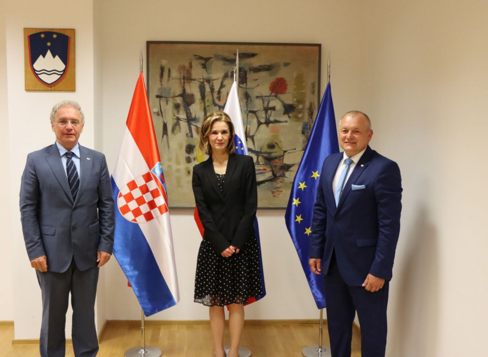 Minister za notranje zadeve Aleš Hojs, državna sekretarka MUP Hrvaške Terezija Gras in državni sekretar Franc Kangler stojijo pred zastavami v sejni sobi.