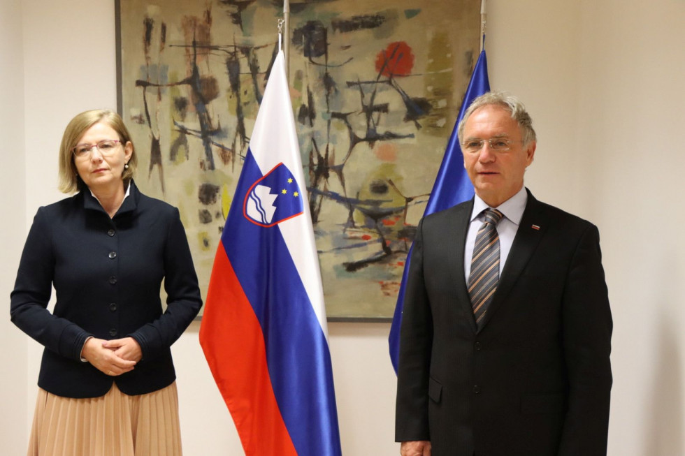 Veleposlanica Madžarske Edit Szilagyine Batorfi in notranji minister Aleš Hojs stojite pred zastavami v sejni sobi.