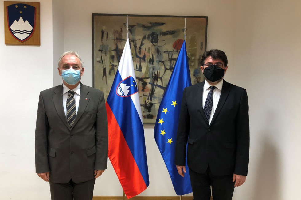 Minister za notranje zadeve Aleš Hojs in veleposlanik Romunije Anton Niculescu stojita pred zastavami v sejni sobi.