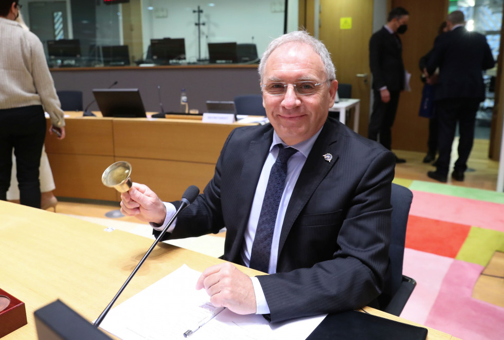 Minister Aleš Hojs sedi za mizo, v roki drži zvonec, s katerim daje signal za začetek srečanja