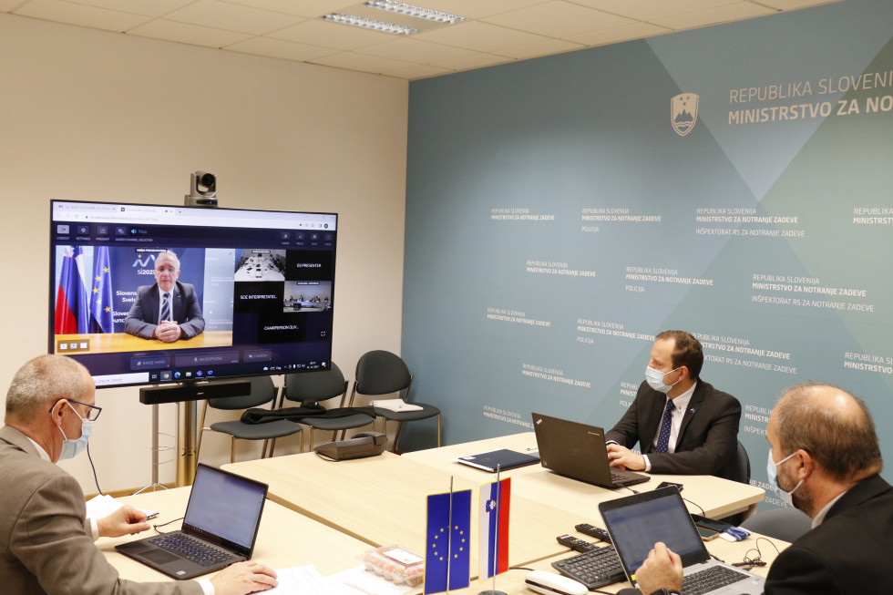 Predstavniki slovenske delegacije sedijo za mizo in gledajo v zaslon