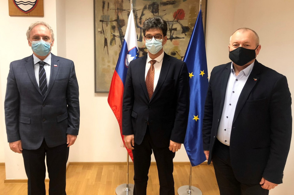 Minister za notranje zadeve Aleš Hojs, državni sekretar Franc Kangler in varuh človekovih pravic Peter Svetina stojijo pred zastavami v sejni sobi.