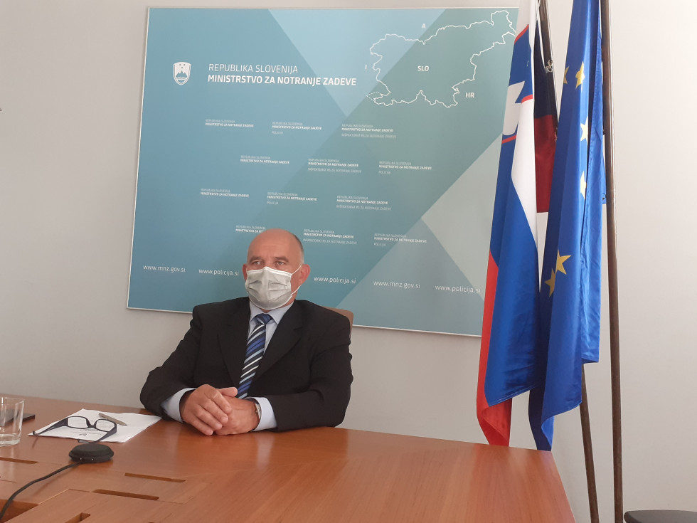 Državni sekretar Božo Predalič sedi za mizo in posluša razpravo na konferenci, ki je potekala preko video povezave