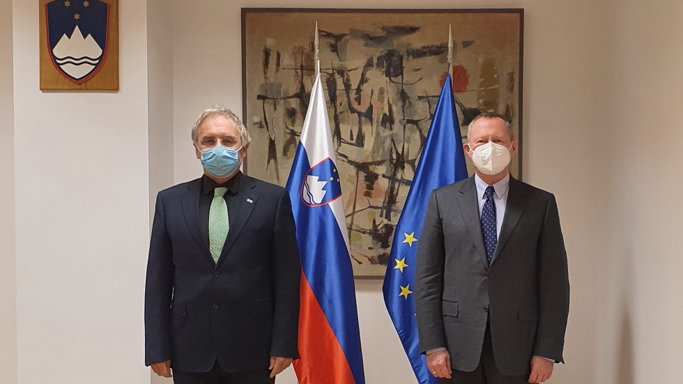 Minister Aleš Hojs in direktor agencije FRA Michael O'Flaherty stojita pred zastavami