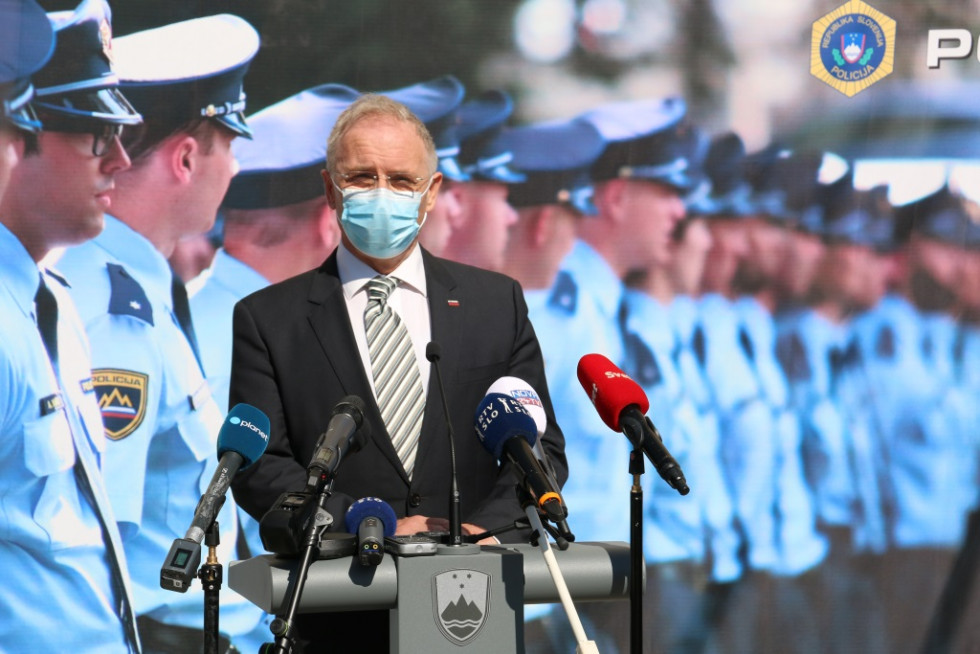 Minister Aleš Hojs stoji pred govornico, v ozadju pano s sliko policistov.