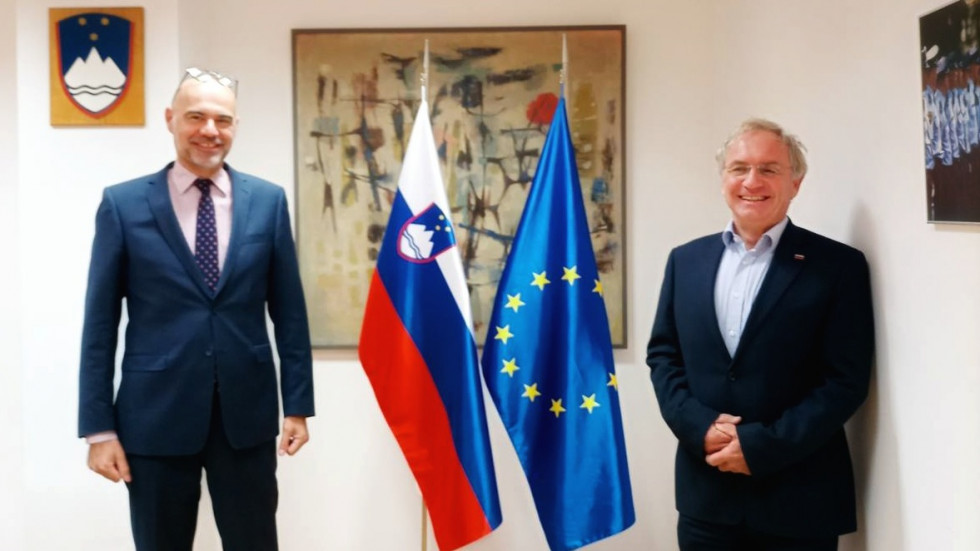 Na levi strani stoji nizozemski veleposlanik, na desni strani minister, za njima zastavi Slovenije in EU