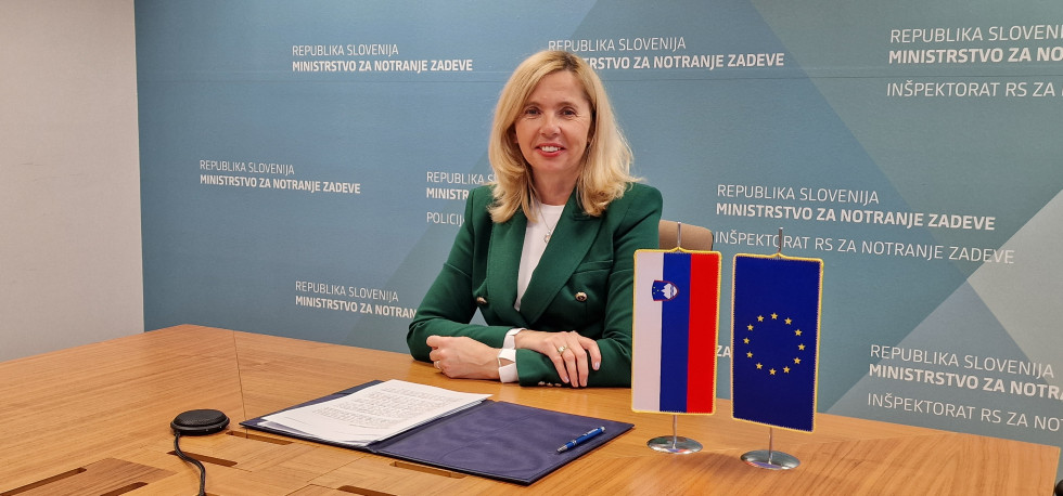 Ministrica za notranje zadeve mag. Tatjana Bobnar na virtualnem forumu o trajni preselitvi, sedi za mizo in gleda v ekran