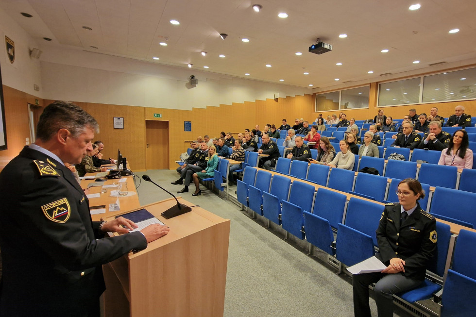 Predavalnica, občinstvo sedi na modrih stolih, spredaj za govornico namestnik generalnega direktorja policije.