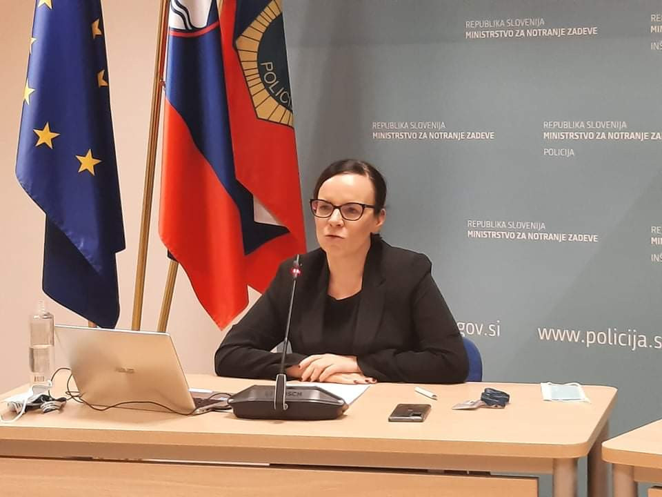 Generalna direktorica Direktorata za migracije Nataša Potočnik, sedi za mizo pred mikrofonom, zadaj zastave