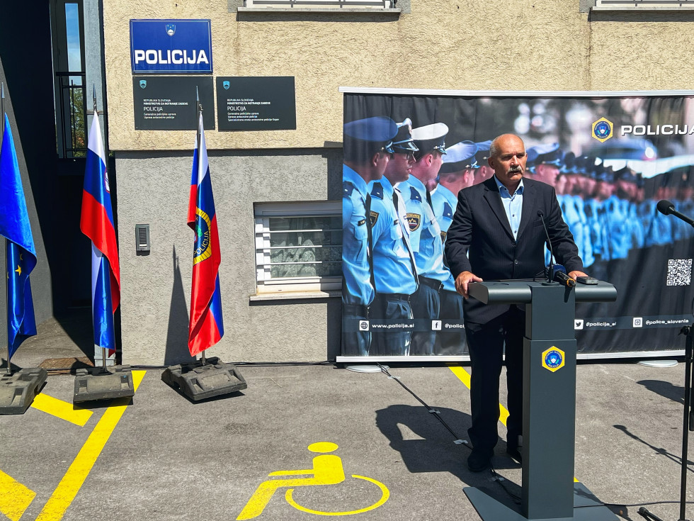 Nagovor državnega sekretarja dr. Boža Predaliča, ki stoji za govornico, na slovesnosti ob odprtju specializirane enote avtocestne policije v Kopru; za njim zastave