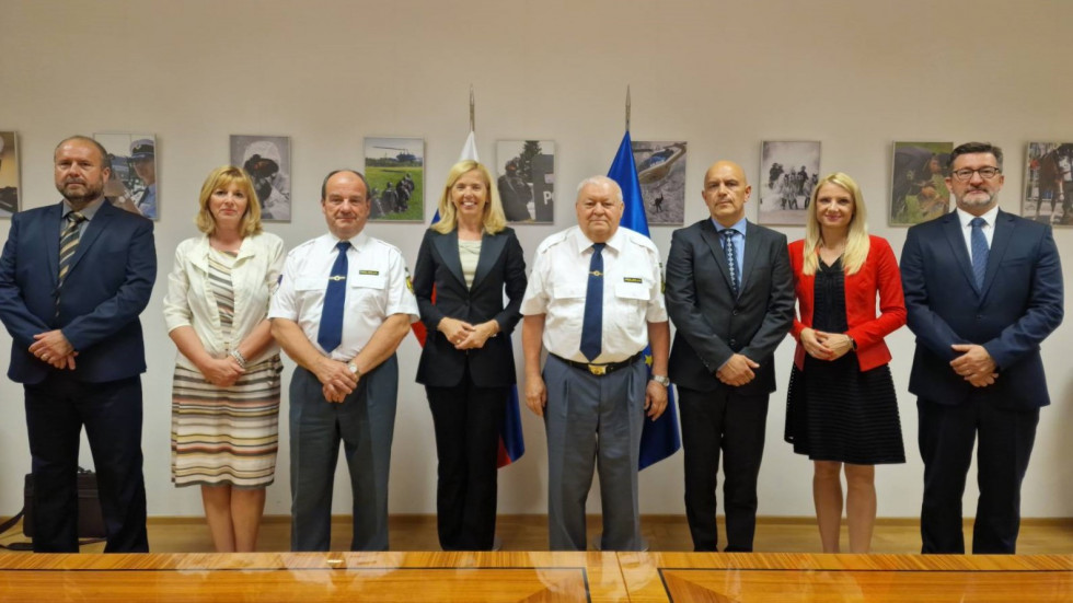 Slavko Koroš, Darinka Sfiligoj, Anton Pozvek, mag. Tatjana Bobnar, dr. Tomaž Čas. mag. Boštjan Lindav, Tina Heferle in dr. Branko Lobnikar. Stojijo pred zastavami, na steni fotografije policije.