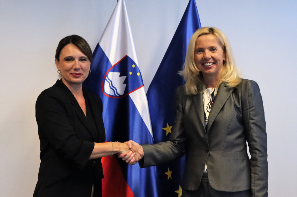 Ministrica za notranje zadeve mag. Tatjana Bobnar in izvršna direktorica Agencije EU za azil Nina Gregori se rokujeta, za njima slovenska in evropska zastava