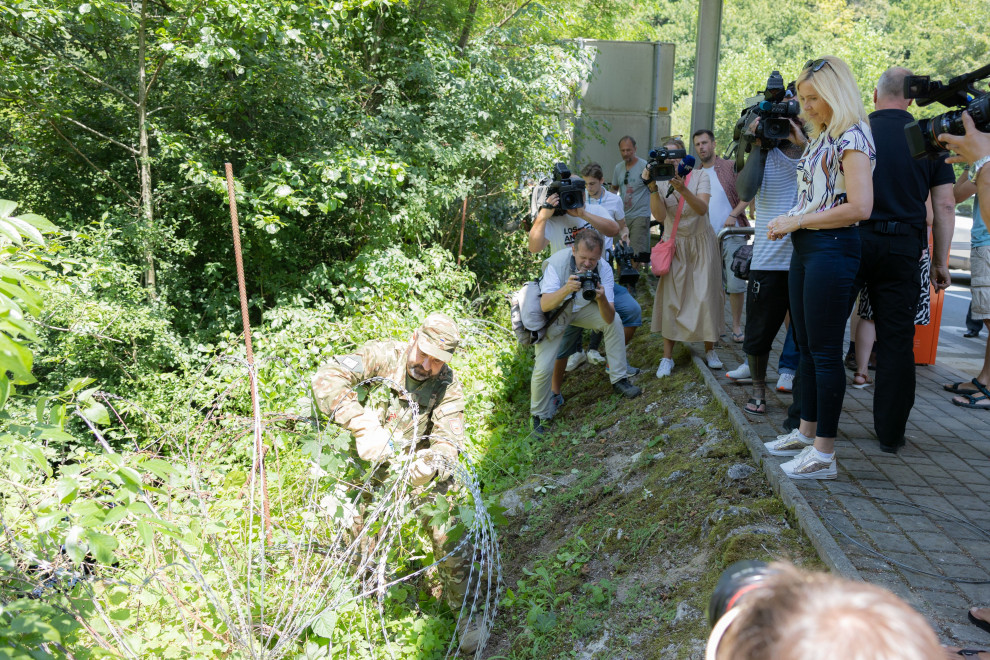Slovenska vojska odstranjuje žičnato ograjo na meji s Hrvaško, za njimi stojijo ministrica in novinarji ki gledajo dogajanje