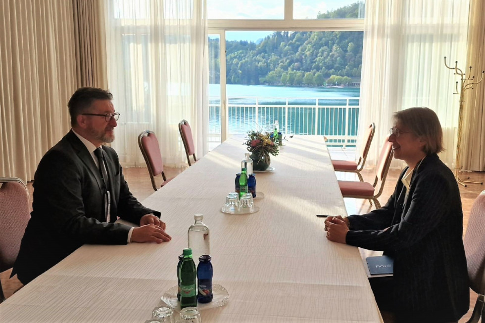 Srečanje državnega sekretarja dr. Branka Lobnikarja in Elise Tsakiri iz Regionalnega urada Mednarodne organizacije za migracije; sedita za mizo, v ozadju pogled na Blejsko jezero.