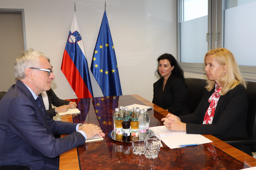 Predstavniki Visokega komisariata Združenih narodov za begunce in ministrstva na sestanku, sedijo za mizo, ob mizi slovenska in evropska zastava