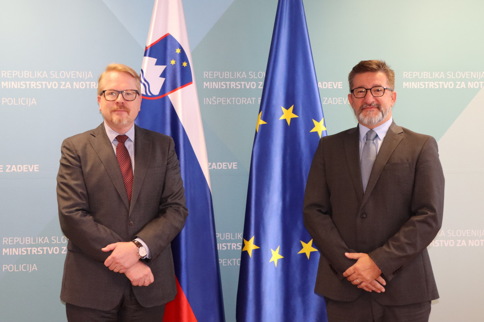 Koordinator EU za boj proti terorizmu Ilkka Salmi in državni sekretar dr. Branko Lobnikar stojita pred evropsko in slovensko zastavo