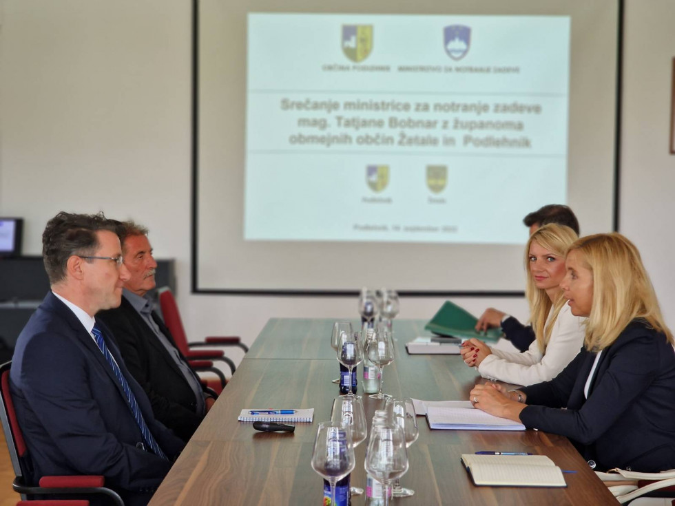  Sestanek ministrice za notranje zadeve z županoma občin Podlehnik in Žetale, sedijo nasproti za sejno mizo, zadaj projekcija z napisom sestanka.