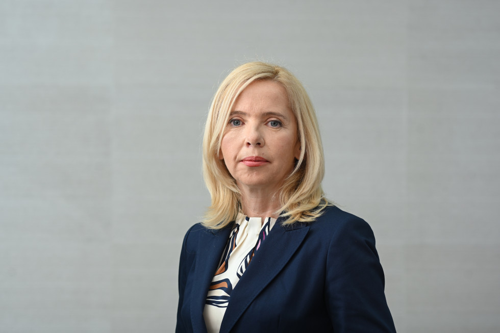 Ministrica za notranje zadeve mag. Tatjana Bobnar stoji, za njo sivo ozadje, ona oblečena v belo majico, z jakno v temno modri barvi 