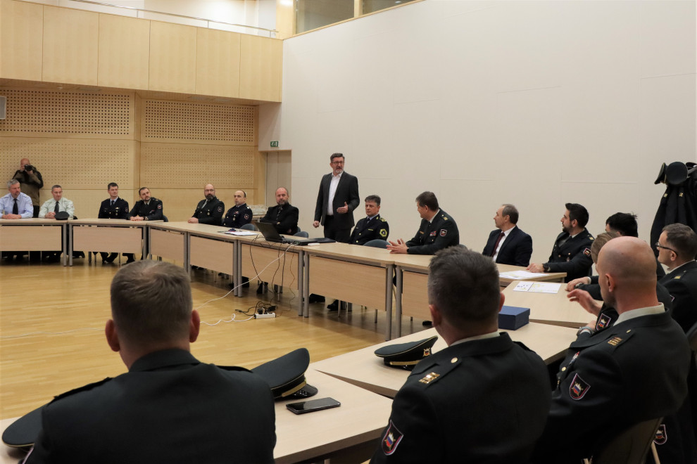 Uvodni pozdrav državnega sekretarja dr. Branka Lobnikarja. On stoji, častniki sedijo za mizami v dvorani.