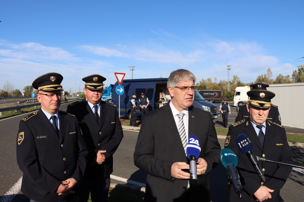 Izjava ministra za notranje zadeve Boštjana Poklukarja na mejnem prehodu Pince. Stoji na prostem pred mikrofoni, ob njem policisti. Modro nebo.