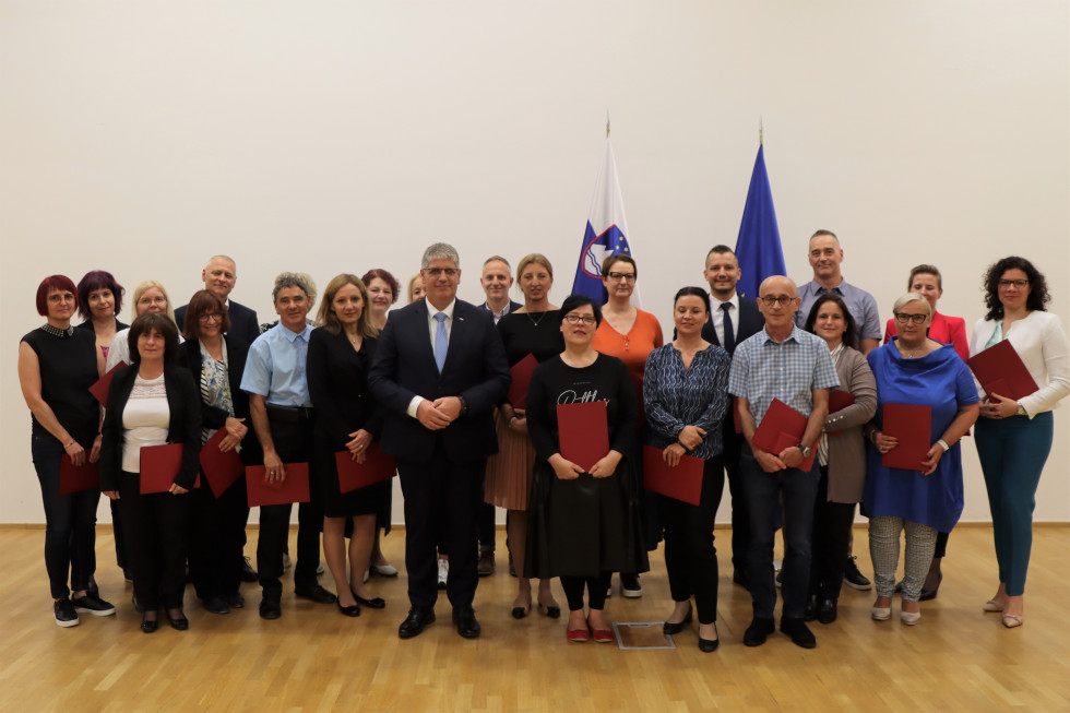 Prejemniki priznanj stojijo in se fotografirajo, za njimi slovenska in evropska zastava