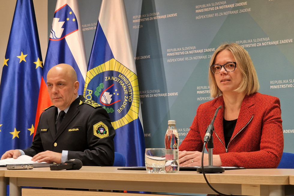 Ministrica za javno upravo v funkciji ministrice za notranje zadeve Sanja Ajanović Hovnik in vršilec dolžnosti generalnega direktorja policije mag. Boštjan Lindav. Sedita za mizo, zadaj moder pano, levo slovenska in policijska zastava.
