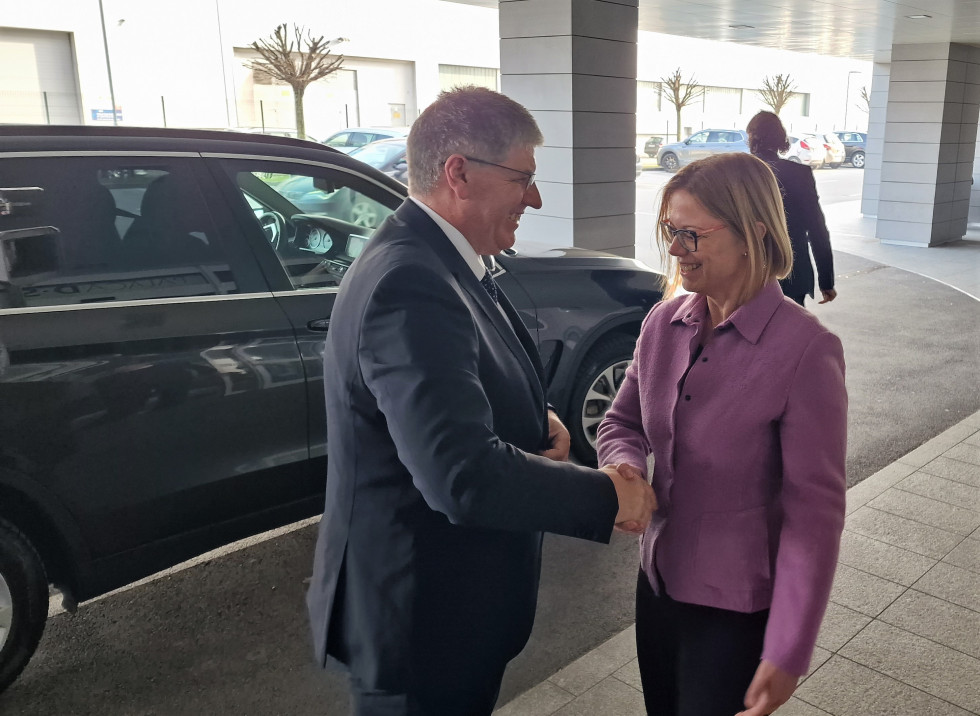 Minister of Public Administration Sanja Ajanović Hovnik and the new Minister Boštjan Poklukar. Shaking hands in fornt of the building's entrance. A black car in the back.