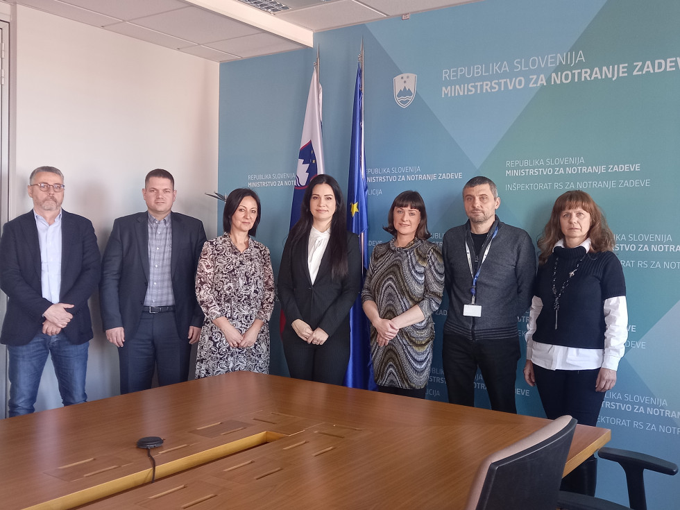 Predstavniki slovenskega in srbskega ministrstva stojijo pred rjavo mizo, za njimi zastavi Slovenije in Evropske unije ter modro ozadje s slovenskim grbom in napisom Republika Slovenija, Ministrstvo za notranje zadeve.