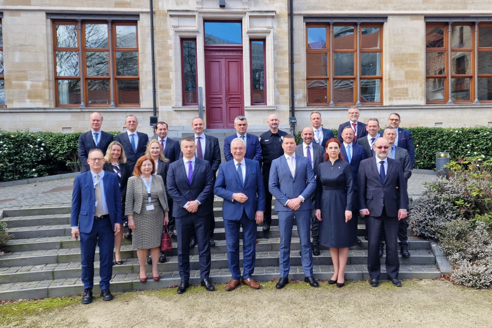 Skupinska slika udeležencev konference. Približno dvajset žensk in moških stoji na stopnicah. Za njimi stavba z rdečimi vrati in rjavimi okni.