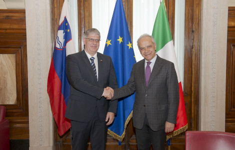 Ministra Boštjan Poklukar in Matteo Piantedosi (Ministers Boštjan Poklukar and Matteo Piantedosi stand in front of the flags of Slovenia, the European Union and Italy and shake hands.)