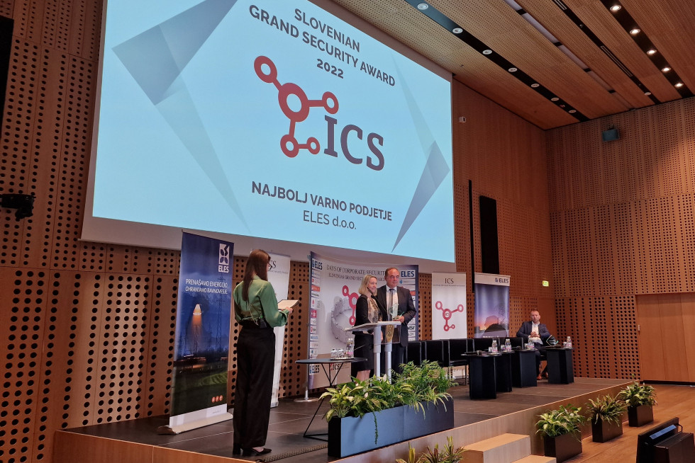 Podelitev nagrade Slovenska velika nagrada varnosti. Na odru stojijo moderatorka, državna sekretarka in predstavnik podjetja Eles. Na njimi velik pano z napisom ICS in naslovom konference.