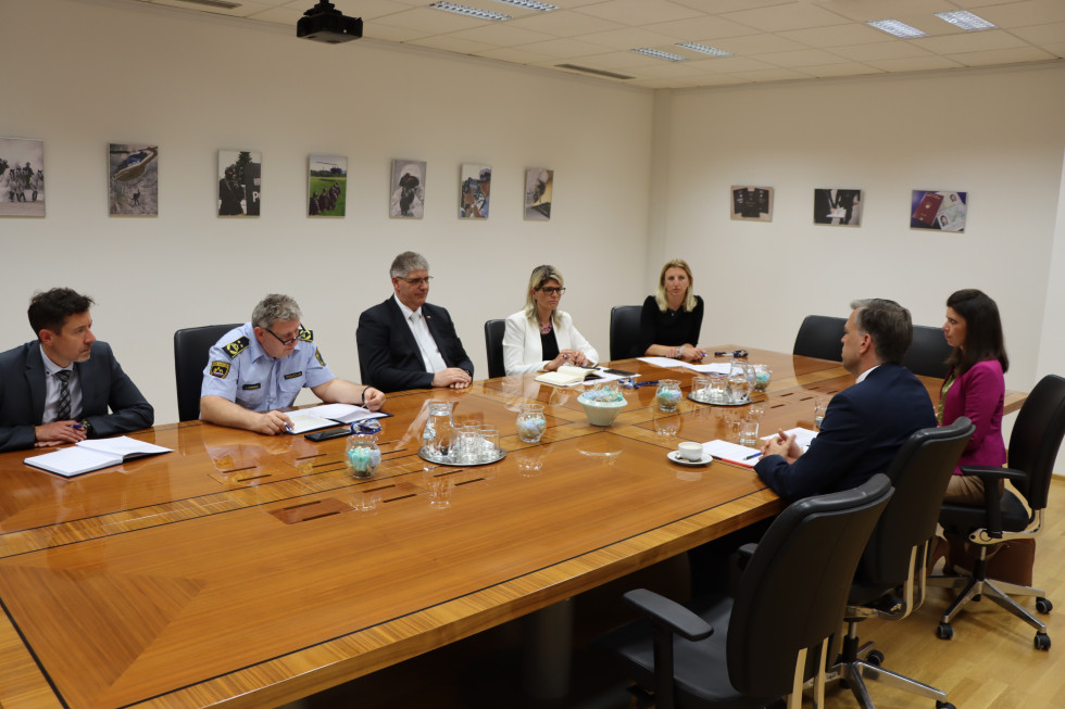 Sestanek vodstva ministrstva in policije z županom Mestne občine Novo mesto. Sedijo za svetlo rjavo sejno mizo. Okrog sta beli steni z manjšimi fotografijami dela policije.