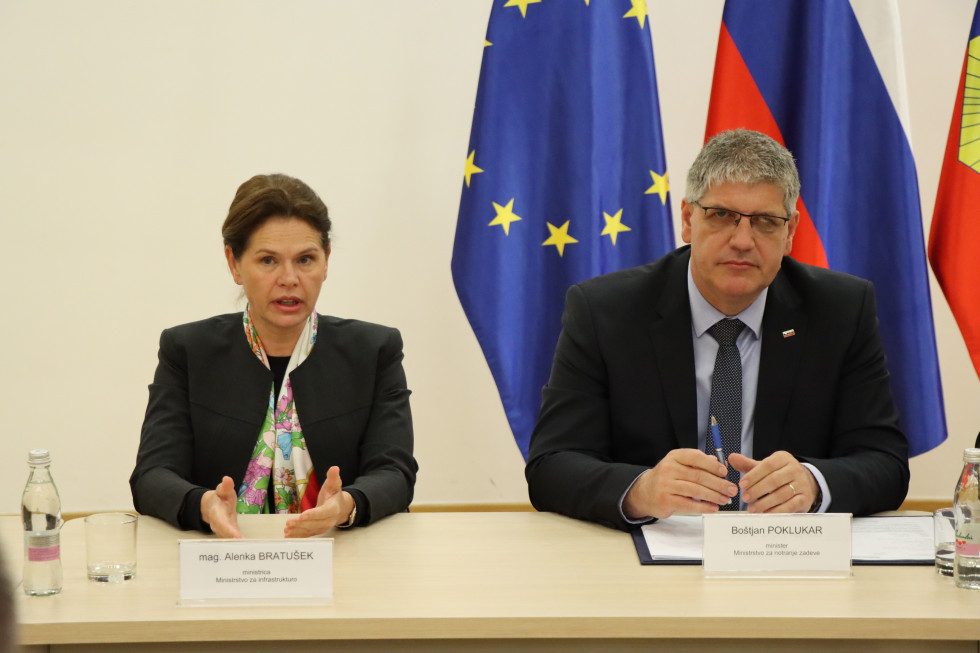 Ministrica za infrastrukturo mag. Alenka Bratušek in minister za notranje zadeve Boštjan Poklukar sedita za mizo. Zadaj zastava EU, slovenska in policijska.