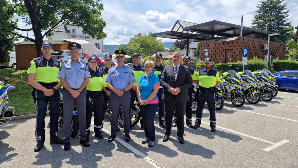 Skupinska fotografija ministra Boštjana Poklukarja, predsednice Nataše Pirc Musar in zaposlenih v policiji. Stojijo na asfaltnih tleh. Za njimi zelena drevesa in rjava stavba.