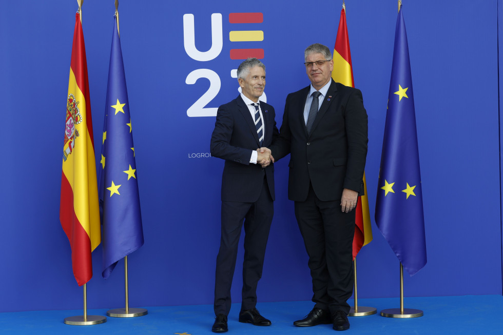 Ministers of Slovenia and Spain are standing on a blue floor, the background is also blue and has the logo of the Spanish Presidency, written EU23 on it. On their left and right are the flags of the European Union and Spain.