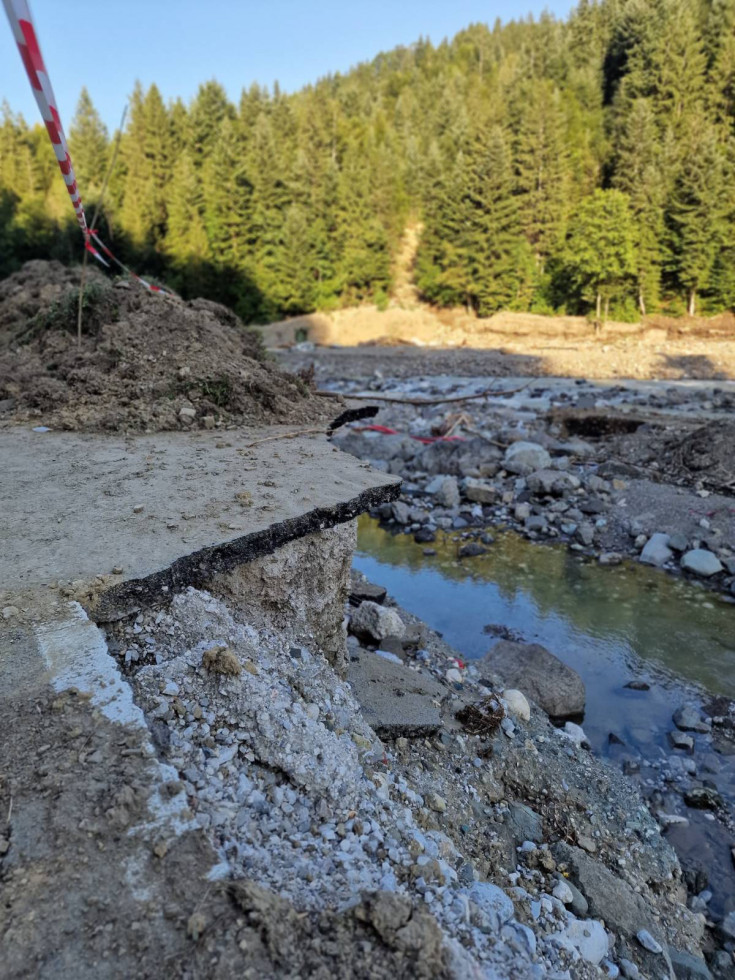Poplavljena cesta, ki je pol manjka, pod njo blatna struga reke