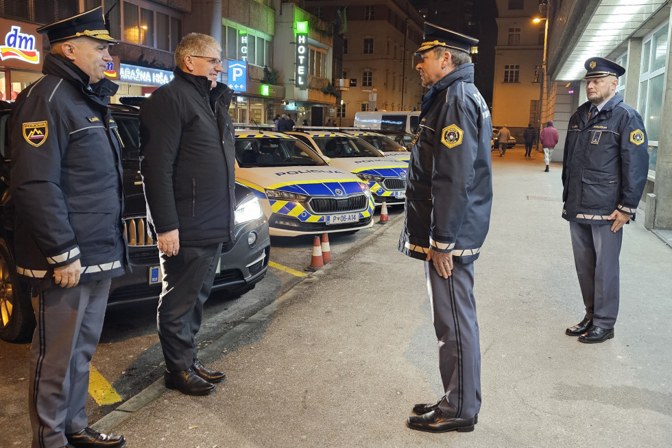 Noč, stojijo na pločniku pred stavbo, v ozadju so policijska vozila.