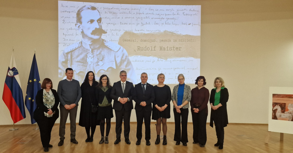 Umetniki, minister in generalni direktor policije stojijo v dvorani, v ozadju projekcija s podobo Rudolfa Maistra